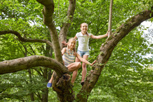 Two Happy Girls Climbing Up Tree In Summer Park