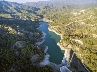 Aerial view of the embankment (earthfill / rockfill) dam in Arminou,Paphos,Cyprus. A terrain reservoir of the river Diarizos in Pafos cutting through the green valley and lush forest of Laona mountain