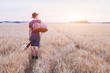 young son leaving home, romantic travel background, man with guitar and road bag walking at sunset field