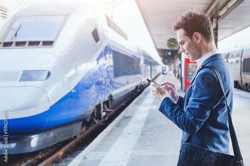 Fotografie, Obraz man using mobile application on his smartphone at train station, business travel