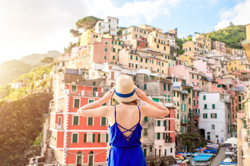 Young female traveler in blue dress enjoying great view on the old coastal town in Riomaggiore on the northern Italy