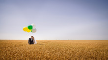 Happy Wedding Couple Stands In The Field Of Wheat Holding Colorf