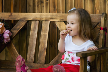 beautiful little girl sitting on a wooden bench and have a cookies