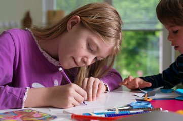 Cute blonde girl drawing with color pencils while her brother or friend observe. Supporting creativity, art.