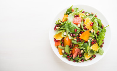 Fresh salad with fruits and greens on white wooden background top view with space for text. Healthy food.