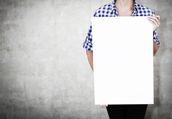 Girl in checkered shirt with poster near concrete wall