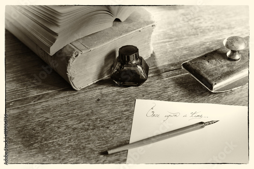 Fototapeta dla dzieci Phrase “Once upon a time” handwritten, surrounded with a fountain pen, an ink pot, a blotting paper holder and old books. Selective focus. Grain noise added. Post processed to look like an old photo.