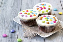 Cupcakes With White Icing And Colored Smarties On The Plate, Wooden Background