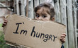 Leinwandbild Motiv Little girl holding a sheet of cardboard. On the cardboard label "I am hungry." The child is three years.
