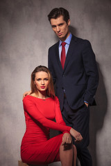 Poster - elegant business man standing behind seated woman in red dress