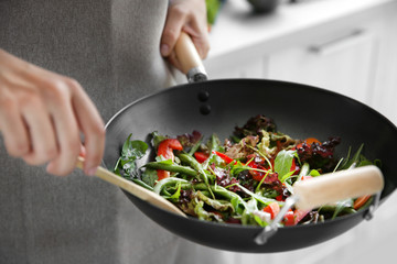 Wall Mural - Female hand mixing vegetables in pan closeup