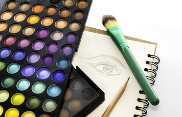 Eye shadow color palette with brush and drawing eye on paper