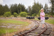 Cute kid boy in straw hat goes on rails,in field, in the summer. Child walking along old railroad.