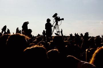 silhouette of cameraman operator shooting a live rock concert, fans around raised hands