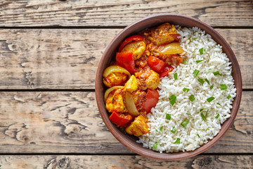 Chicken jalfrezi Indian spicy curry chilli meat with basmati rice and vegetables healthy dietetic asian food in clay dish on vintage table background.