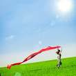 © mr.markin - Beautiful young woman jumping on a green meadow with a colored red tissue. Happy female in wheat field with fabric. Summer picnic and freedom concept.
