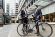 © Sergey Nivens - Two young businessmen with a bike in city centre