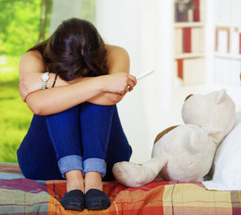 Wall Mural - Pretty young brunette woman resting head in lap crying, bookshelves interior, garden window background