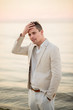 © ronedya - young handsome man in a white suit near the sea at sunset. young handsome groom on the beach. Close-up