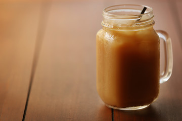 Poster - Iced coffee in glass jar with straw on brown wooden table