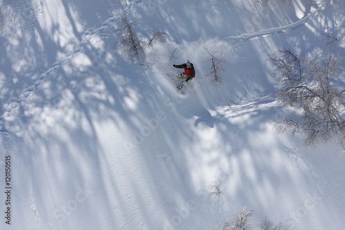 Fotografie, Obraz Snowboarder Carves a Slash While He Rides Down the Snowy Mountain Terrain at the