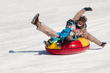 Winter Fun. Young Woman And Little Boy Sliding Downhill On A Snow Tube