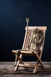 skeleton is gesticulate sitting on the wood chair