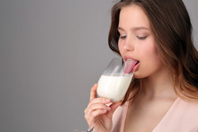 Girl Licking Milk From A Wine Glass. Close Up. Gray Background