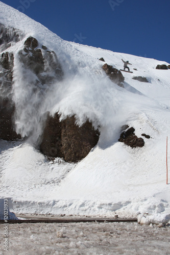 Fotografie, Obraz Snowboarder Does a Big Air Jump Near Some Steep Rock Cliffs