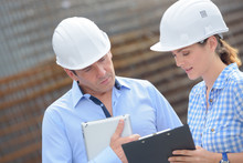Man And Woman In Hardhats Looking At Clipboard