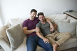 © Picxel Creative - Gay Male Couple On Sofa At Home Watching TV