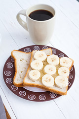 Close-up of breakfast with two sandwiches with honey and banana and cup of black coffee on table