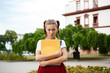 Upset young beautiful female student looking down holding folders outdoors, park background.