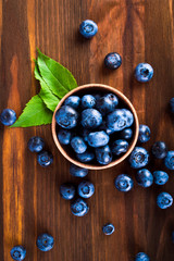 Wall Mural - Blueberry berries in a wooden glass scattered on the wooden table.