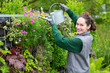 Young attractive woman working in a public garden watering flowe