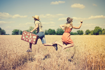 Couple running in field, man holding in his hand vintage suitcase on countryside landscape blue sky outdoors background