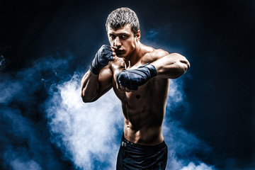 muscular kick-box or muay thai fighter punching in smoke.