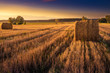 Sun rises over a field of stubble with haystacks. August countryside landscape. Masuria, Poland..