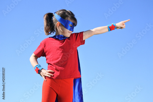 Superhero girl points towards dramatic blue sky Poster Mural XXL