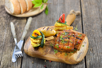 Vegan grillen: Grillteller mit Seitan dazu Zucchini-Röllchen, Grillkartoffel und Ciabatta serviert - Vegetarian grill platter with vegan seitan slices, courgette rolls and grilled potato