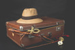 Travel and adventure concept. Vintage brown suitcase with fedora hat, bullwhip, compass and ankh key of life on dark background