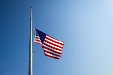 American Flag Flies At Half Mast Backlit By The Sun In Bright Blue Sky