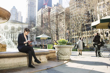 Businesswoman Using Tablet While Sitting Against Fountain At Bryant Park
