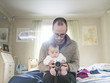 © Astrakan Images - Father and daughter holding camera while sitting on bed at home