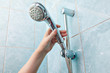 Close-up of human hand adjusts holder shower head with hose.