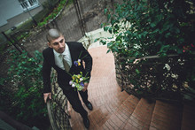 Happy Groom Climbing Up Stairs And Holding Wedding Bouquet