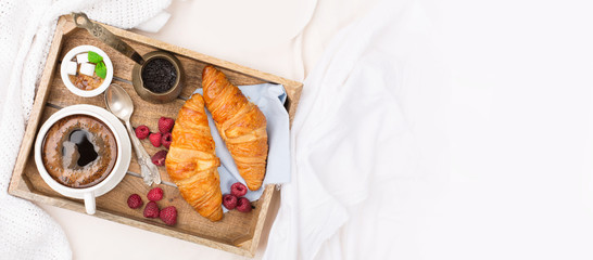 Wall Mural - Morning breakfast in bed with cup of coffee, croissants, fresh berries and honey on wooden tray, selective focus