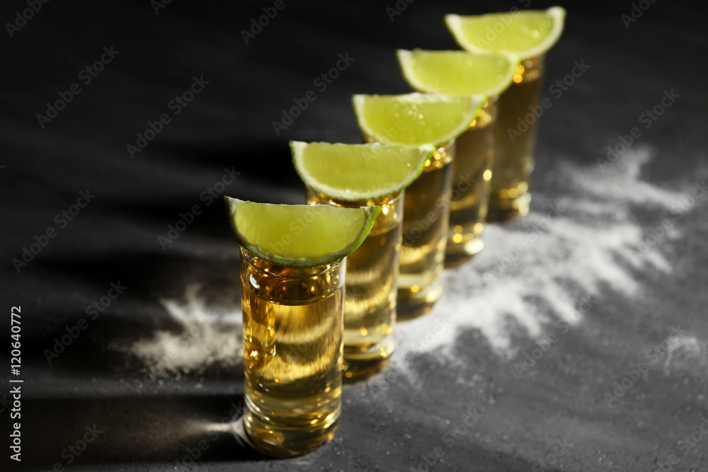 Gold tequila shots with lime and salt on gray background