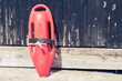 Close up of red lifeguard rescue can equipment against the wooden tower wall at the sandy beach. 