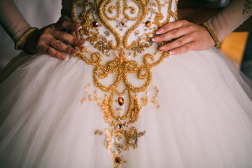 Bride in crown sitting in a beautiful white dress decorated yellow beads, hands with a wedding ring with a jewel of a close-up. Morning of the bride. Wedding day.  